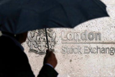 A man shelters under an umbrella as he walks past the London Stock Exchange in London, August 24, 2015.