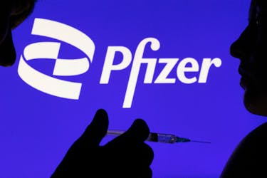 People pose with syringe with needle in front of displayed Pfizer logo in this illustration taken, December 11, 2021.