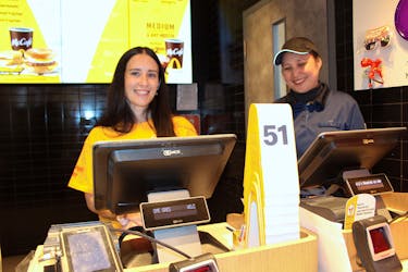 Laura MacPhail, of Coldwell Banker Boardwalk Realty, is shown behind the counter of McDonald’s in Sydney River took orders under the watchful eye of McDonald’s employee Celeste Yu.