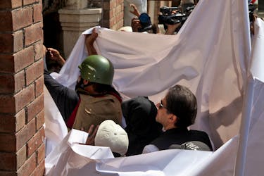 Pakistan's former Prime Minister Imran Khan and his wife Bushra Bibi are covered with a white sheet as they arrive to appear at the High Court in Lahore, Pakistan, May 15, 2023.