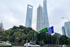 Cars travel past a display showing Shanghai and Shenzhen stock indexes near the Shanghai Tower and other skyscrapers at the Lujiazui financial district in Shanghai, China February 5, 2024.