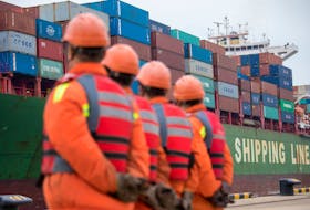 Workers look on as a cargo ship approaches a terminal at the port of Qingdao in Shandong province, China November 8, 2018.