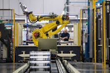 A factory worker works on an aircraft part, as the robot arm of an automated five-axis cell operates autonomously nearby, at Abipa Canada, in Boisbriand, Quebec, Canada May 10, 2023.