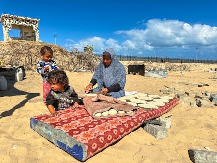 A woman prepares food next to children, as displaced Palestinians take shelter at the border with Egypt, during an Israeli military operation, in Rafah in the southern Gaza Strip, May 29, 2024.