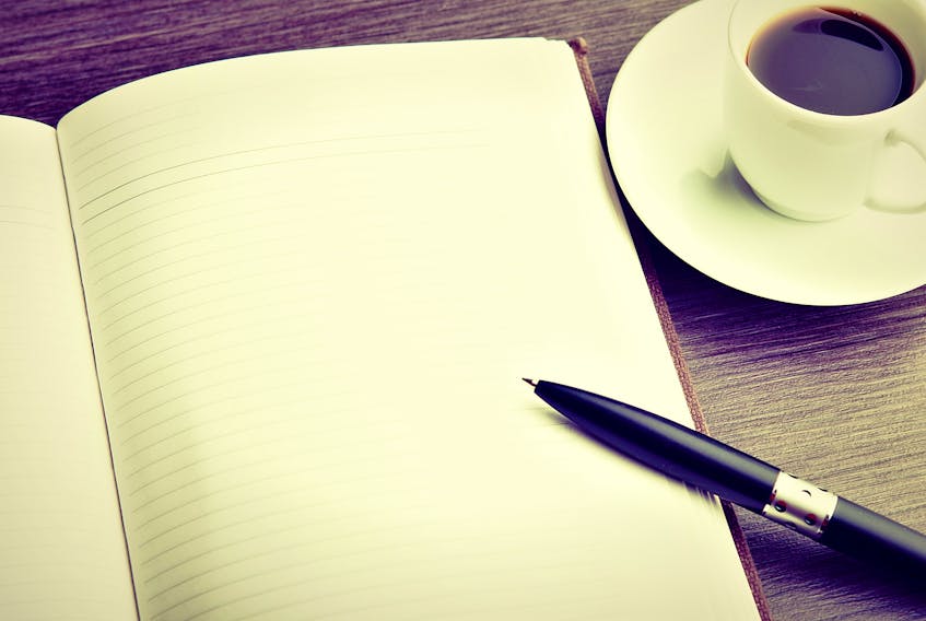 Stock image of an open notebook and pen on a wooden table with a cup of coffee.