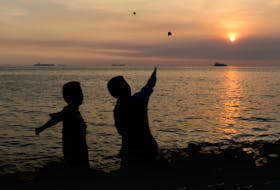 Two children skip a stone into the sea at sunset.