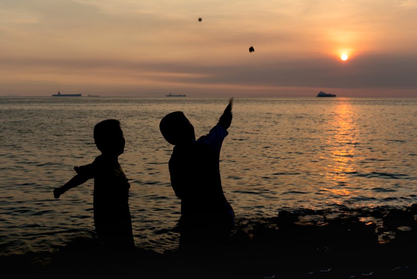 Two children skip a stone into the sea at sunset.
