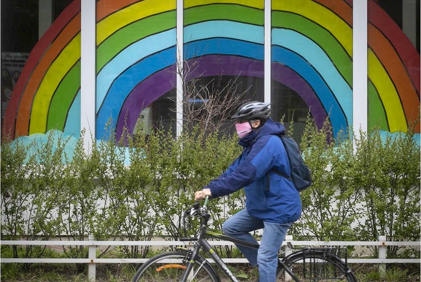 A cyclist wearing a mask rolls by a rainbow painted on a window on Sherbrooke St. on Tuesday, May 5, 2020. 