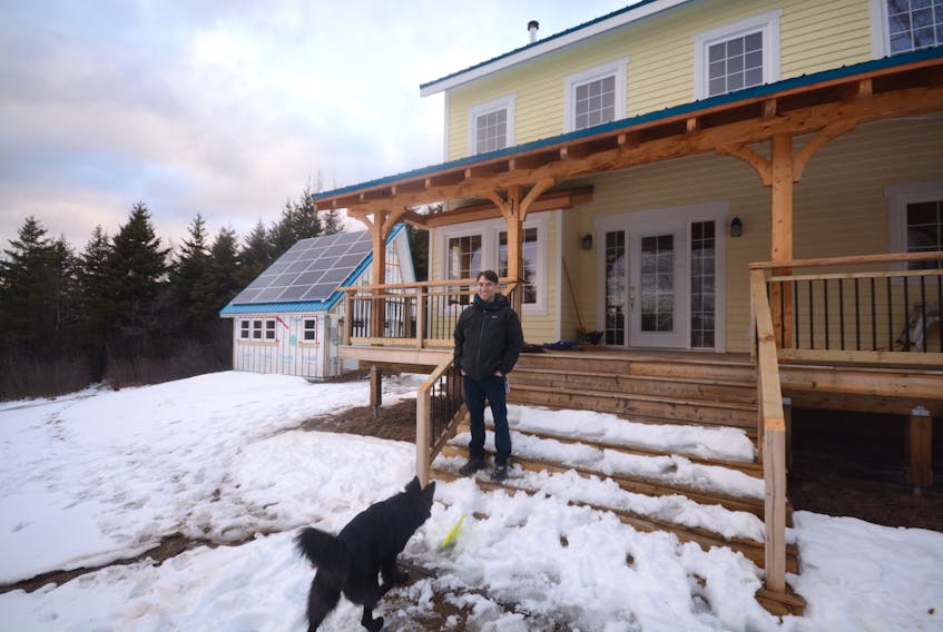 Jason Blanch plays Frisbee with his dog outside his off-grid home in Upper Nappan. The 20 solar panels on top of the garage provide power to the home.