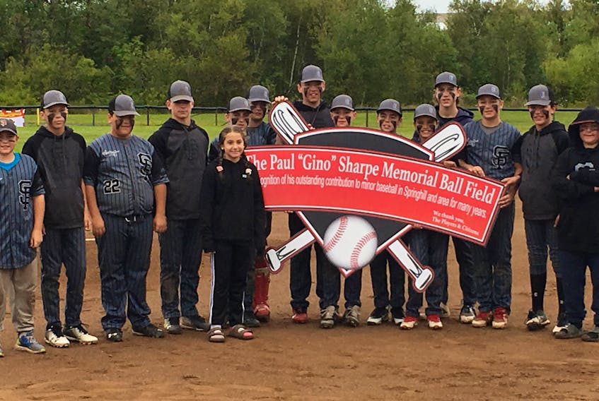 Julia Sharpe stands with members of the Springhill 13U AA Fencebusters during the unveiling of a sign that renames the Fencebusters Field the Paul ‘Gino’ Sharpe Memorial Field. The ceremony was held prior to the championship game at the Atlantic 13U AA Baseball Championships on Sept. 15.