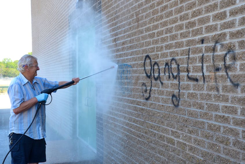 Lawrence Moody uses a power washer to blast away graffiti on the back wall of the Annapolis East Elementary School in Middleton July 16. He and Cheryl Nogler, school custodial staff, spent the entire day getting rid of 52 separate instances of graffiti on the school walls.