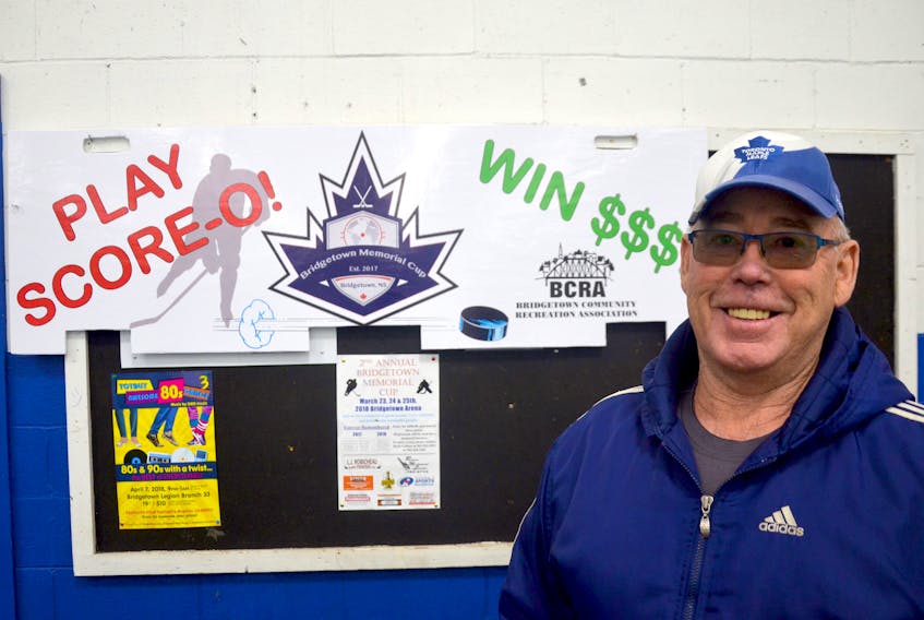 Steve Clayton stands in front of the Score-o board that will be placed across the net between periods during the Sunday championship game of the second annual Bridgetown Memorial Cup. Tickets are being sold for $5 each by members of the BRCS senior girls hockey team. If your ticket is drawn you get a chance to take a shot and win $500.