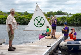 Extinction Rebellion’s Nina Newington, a horticulturalist, stands on the floating dock at Jubilee Park in Bridgetown July 13 during the Annapolis River Festival. She’s a member of Extinction Rebellion Forest Protectors and is demanding a halt to deforestation and praising the idea of planting one trillion trees to help slow climate change. XR member Ian Currie gets into the XR pink canoe.