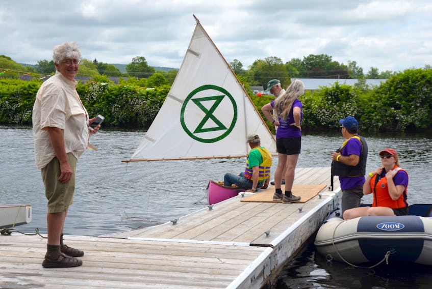 Extinction Rebellion’s Nina Newington, a horticulturalist, stands on the floating dock at Jubilee Park in Bridgetown July 13 during the Annapolis River Festival. She’s a member of Extinction Rebellion Forest Protectors and is demanding a halt to deforestation and praising the idea of planting one trillion trees to help slow climate change. XR member Ian Currie gets into the XR pink canoe.