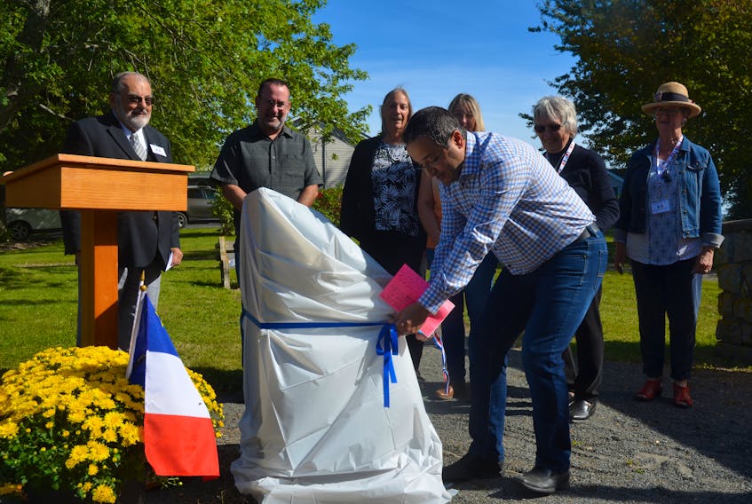 Warden Abraham Zebian, representing West Hants, does the honours cutting a ribbon to reveal a monument marking Sainte-Famille Cemetery in Falmouth.