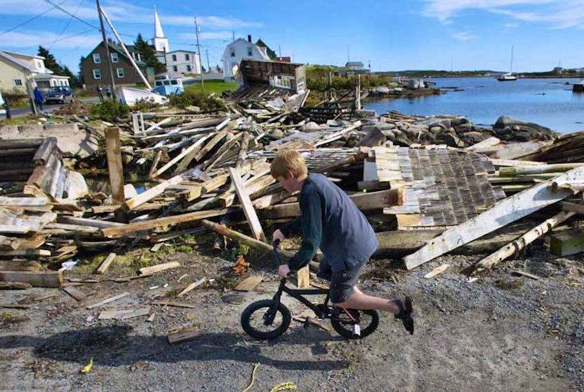 A youngster rides his bike in front of the wood from shattered wharves in Prospect Village, Wednesday. The small fishing community lost all of its wharves during hurricane Juan's passage.