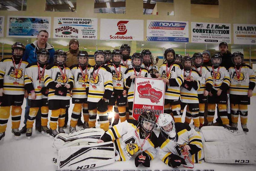 The Atom ‘A’ Antigonish Bulldogs female team celebrates with the banner and medals they earned.