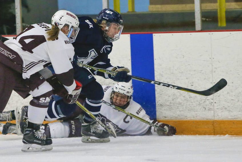 
St. Francis Xavier X-Women’s Kristen McKinley, centre, tips the puck up the ice while on a rush between Saint Mary’s Huskies’ Taylor Keeping, left and Kiana Wilkinson during AUS women’s hockey action in Halifax on Thursday. - Tim Krochak
