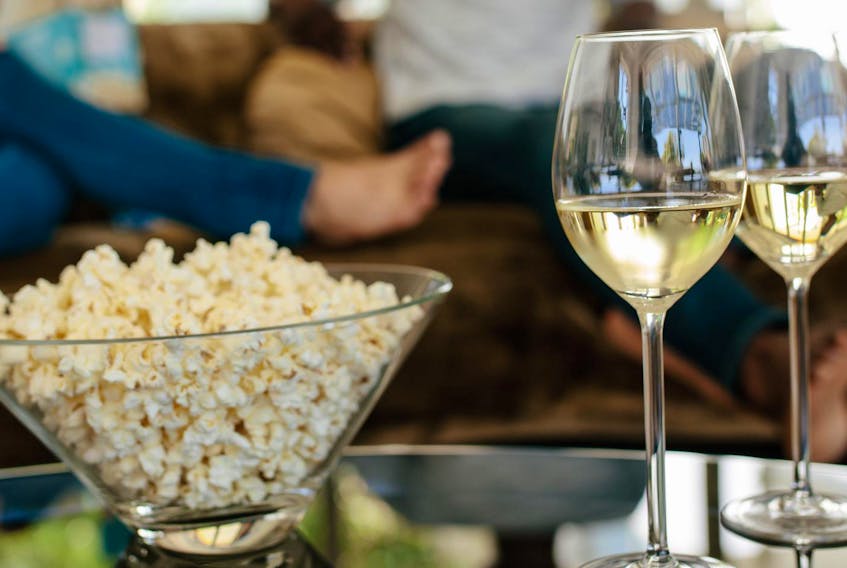 
Bowl of popcorn and wine glasses on table in front with couple sitting and relaxing on couch in background. - Jacob Ammentorp Lund
