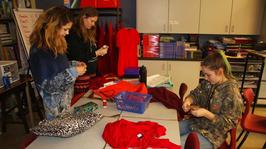 
Students, left to right, Raven Harris, Dallas Weare and Emily Rodenhiser attaching the donated Red Dresses to the wooden hangers that will be used to display the project. (Contributed)

