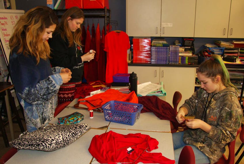 
Students, left to right, Raven Harris, Dallas Weare and Emily Rodenhiser attaching the donated Red Dresses to the wooden hangers that will be used to display the project. (Contributed)
