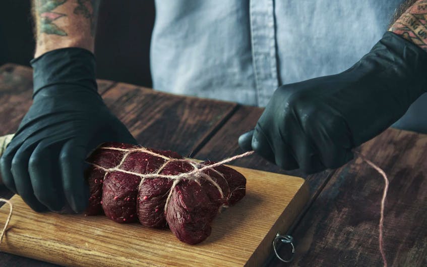 
A butcher ties piece of meat with craft rope to smoke it on wooden aged table. - 123RF
