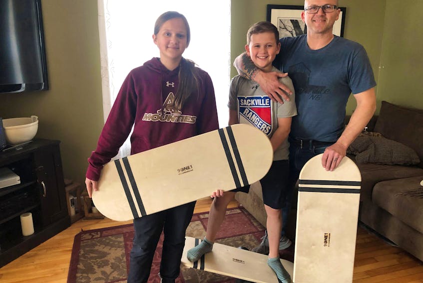 Kevin Alder (right) and his kids Aaron (middle) and Jesse (left) pose with their homemade balance boards. Alder has been making balance boards to sell during quarantine.