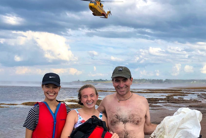 Léonie Bussière, Rowan Blanch and Jason Blanch stand on the beach at Seagrove as a Cormorant helicopter leaves the area after Blanch’s sailboat struck a sandbar and tipped over on Tuesday.