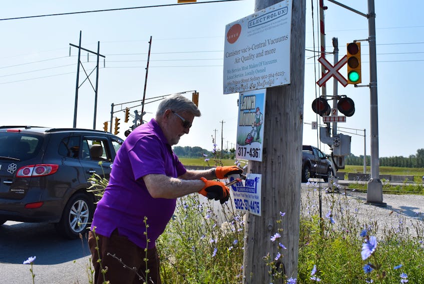 CBRM councillor Jim MacLeod wasted no time in getting to the task of pulling down unauthorized utility pole signs on the first day he has been allowed to do so. Earlier this summer, municipal council gave the go-ahead to proceed with enforcement measures to remove what MacLeod calls “unsightly and disgusting” signage. Above, the Whitney Pier resident and District 12 councillor tears down some signs on a utility pole near the corner of Lingan and SPAR roads in Sydney.
