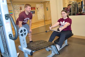 Julia Peck, right, 18, of Louisbourg, gets assistance on the seated cable row from her cousin Jamie Hunt, also from Louisbourg, at the YMCA of Cape Breton.