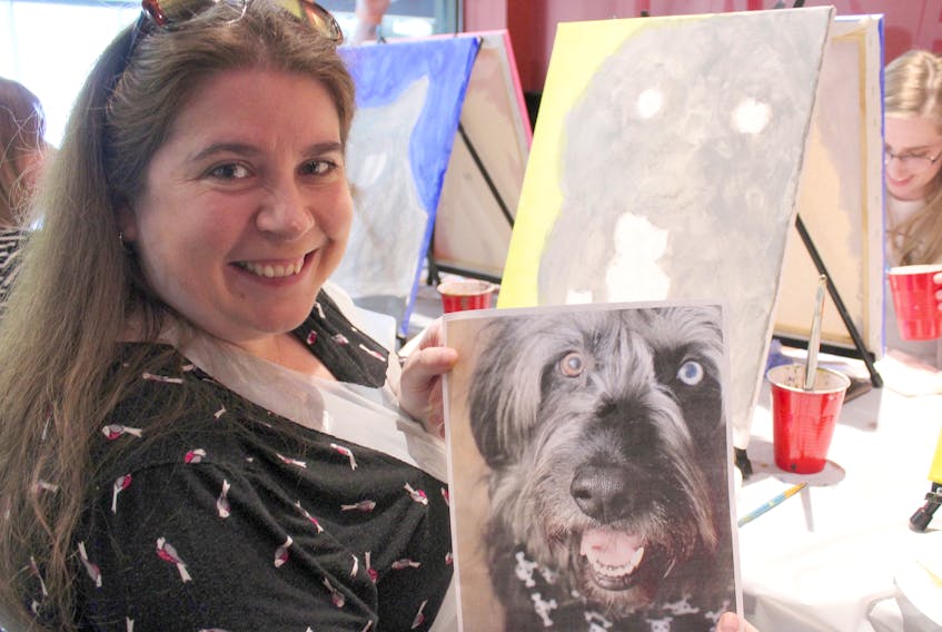 Tracy McLennon holds up a photo of her dog Kya during a paint-your-pet event at Eastside Mario’s in Sydney on Wednesday. The Sydney resident was one of 17 people who took part in the latest event hosted by local artist Steven Rolls. Rolls creates paint-by-number-like canvases using photographs of pets, then leads their owners through the process of painting personalized portrait.