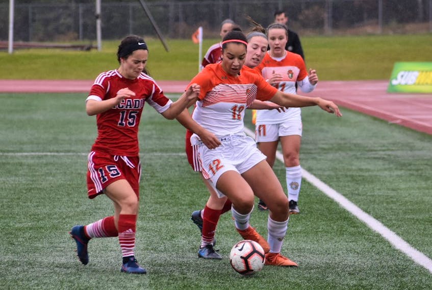 Alliyah Rowe of the Cape Breton Capers, right, carries the ball as she's pressured by Mya Harnish of the Acadia Axewomen during Atlantic University Sport soccer championship at the Cape Breton Health Recreation Complex turf in Sydney on Sunday.