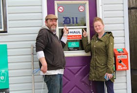 Chuck Ogley, left, and Elizabeth Doyle point to their District 11 Taxi company logo on the front door of their main dispatch office in New Waterford. After their plans to expand service to Sydney and Glace Bay were stopped because of CBRM bylaws, the co-owners decided to open up in Inverness.