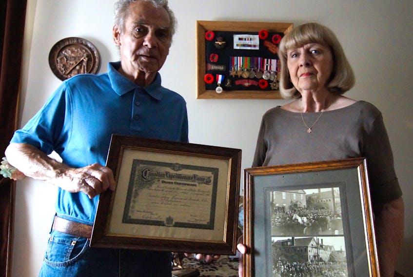 Jim McMullin, and his wife Sharon McMullin, formerly of Glace Bay and now of Winnipeg, hold the death certificate of John Bernard Croak and photos of a parade in Glace Bay in 1918 believed to be in memorial for war hero John Bernard Croak following his death during the First World War. McMullin has spent more than 50 years researching Croak and has written two books about him.