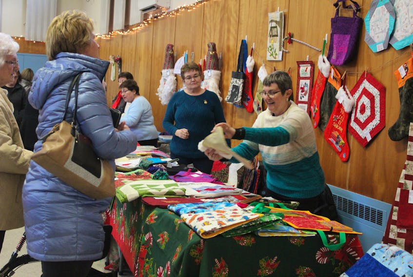 Mary Stewart (back left) watches as her vendor partner Frances Aucoin shows one of their homemade Christmas stockings to a customer during the Last Chance Shopping Event at Sydney Forks Recreation Centre on Dec. 8. The two retired hobby quilters/ crafters said the Christmas market at the centre is the only one they sell at because they like the smaller venue and atmosphere.