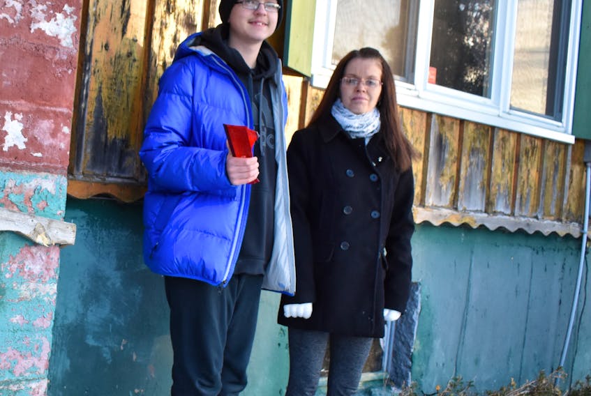 David MacDonald, 13, and his mother, Ollie MacDonald, stand next to the spot on the house that was hit by a car on Friday. He is holding a piece of the broken taillight from the car.