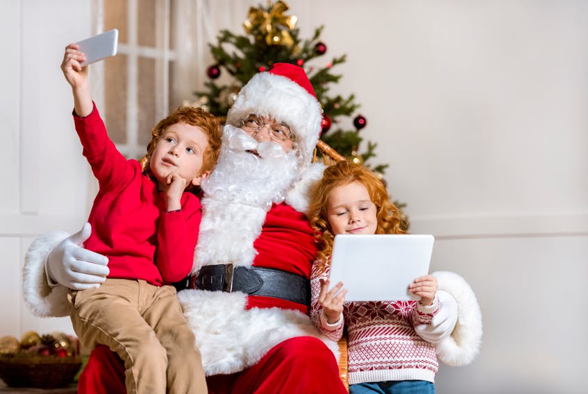 Santa watches as two children play with a smartphone and tablet in this stock photo. The head of a Cape Breton charity that provides Christmas gifts for about 600 struggling families every year, said she agrees with a popular “Not from Santa” Facebook post that urges parents to take credit for expensive gifts that many families can’t afford people can’t afford.  Contributed