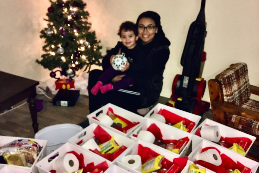 Briana Berardinelli sits with her daughter Rosemary and the boxes of food and necessities that will be available Wednesday, Dec. 18, at the Santa Claus is Coming to Town event at the North Sydney exhibition grounds.
