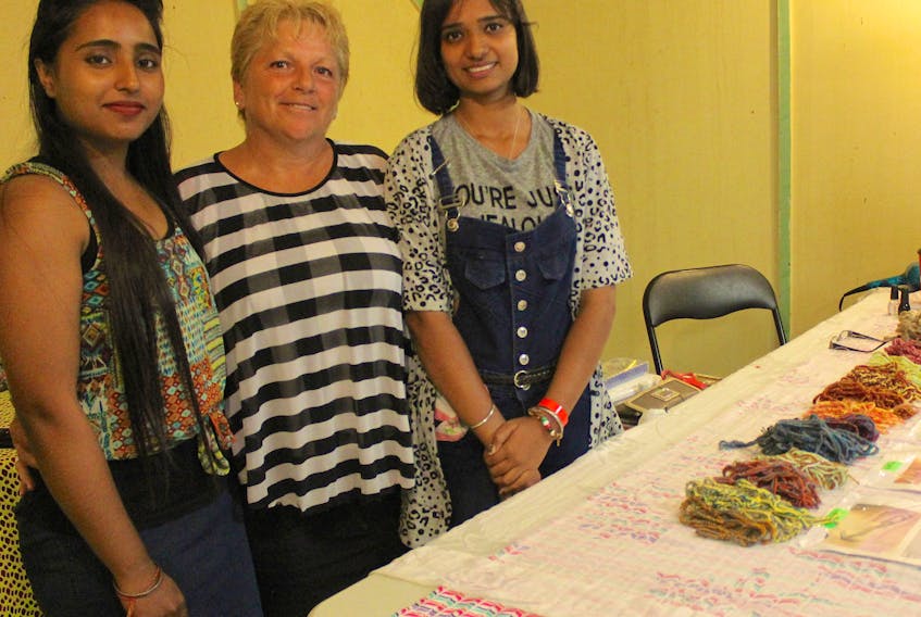 From left, Kamalpreet Kaur, Helen MacDonald and Pavanjit Kaur at the Cape Breton Exhibition in North Sydney on Tuesday. They are standing behind Pavanjit's henna tattoo stand which is set up for the exhibition. Needing to save enough money for tuition, MacDonald suggested Pavanjit start doing mehndi art (henna tattoos) at markets, fairs and private parties. This isn't the only way MacDonald is helping the student from India adjust to life in Canada.