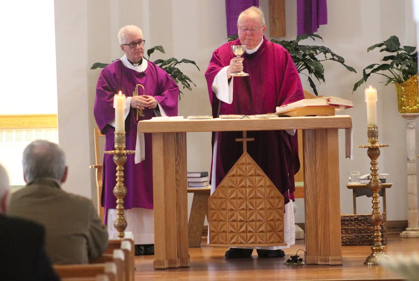 Rev. Bill Burke, right, holds up the chalice holding a liquid that symbolizes the blood of Christ during communion at St. Marguerite Bourgeoys church on Sunday.