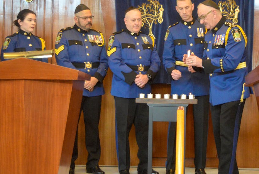 Chief Peter McIsaac, right, shelters a candle during a Holocaust memorial service at the Temple Sons of Israel Synagogue in Sydney on Sunday as Sgt. Erin Donovan, from left, Sgt. Barry Best, Staff-Sgt. Gilbert Boone, Deputy Chief Robert Walsh look on. An estimated crowd of 200 people turned out for the ceremony that featured a keynote address by Dr. Allan Rosenfeld, a Toronto physician whose parents were Holocaust survivors.