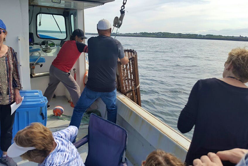 Mary Pat Mombourquette, left, of Glace Bay, executive director of the Cape Breton Miners Museum and a member of the executive for bayitforward, watches as a lobster fisherman brings in a trap, while on an outing on a fishing boat with other community members escorting seven potential doctors and some of their family members around the community on Thursday. Bayitforward has formed a partnership with the Cape Breton Family Medicine Recruitment Committee to help attract potential doctors to Glace Bay by rolling out the red carpet for them and showcasing Glace Bay when they arrive to visit.