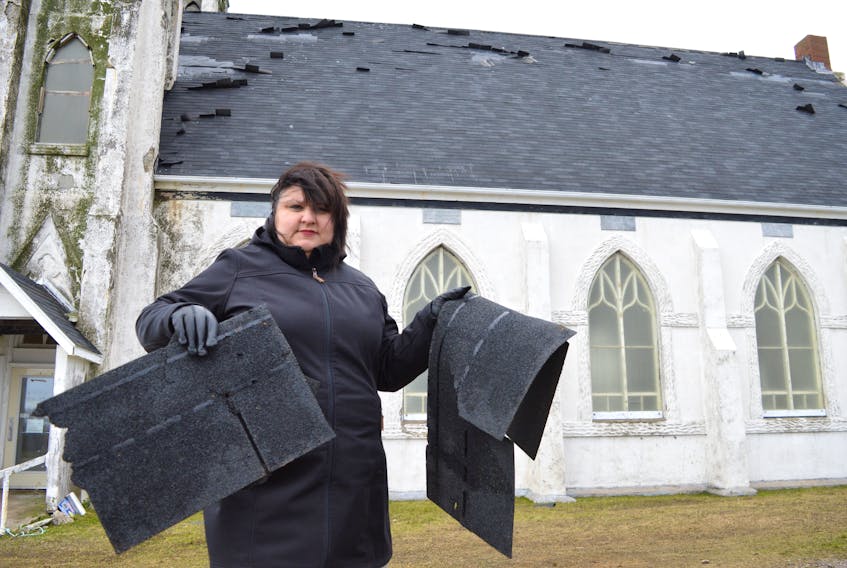 Melanie Sampson, chair of the Stone Church Restoration Society, holds up some of the pieces of shingle found on the ground at the former St. Alphonsus church in Victoria Mines after the new roof was damaged during a wind storm on Thursday. Sharon Montgomery-Dupe/Cape Breton Post