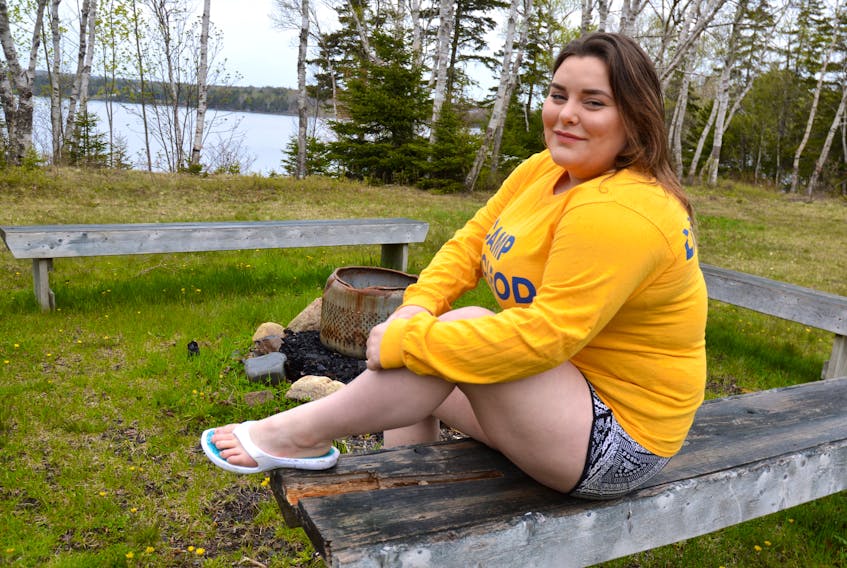 Taylor Maxwell, co-director at Camp MacLeod in Albert Bridge, sits on a bench by the campfire while out checking the premises in preparation for camp this year, which begins July 2.