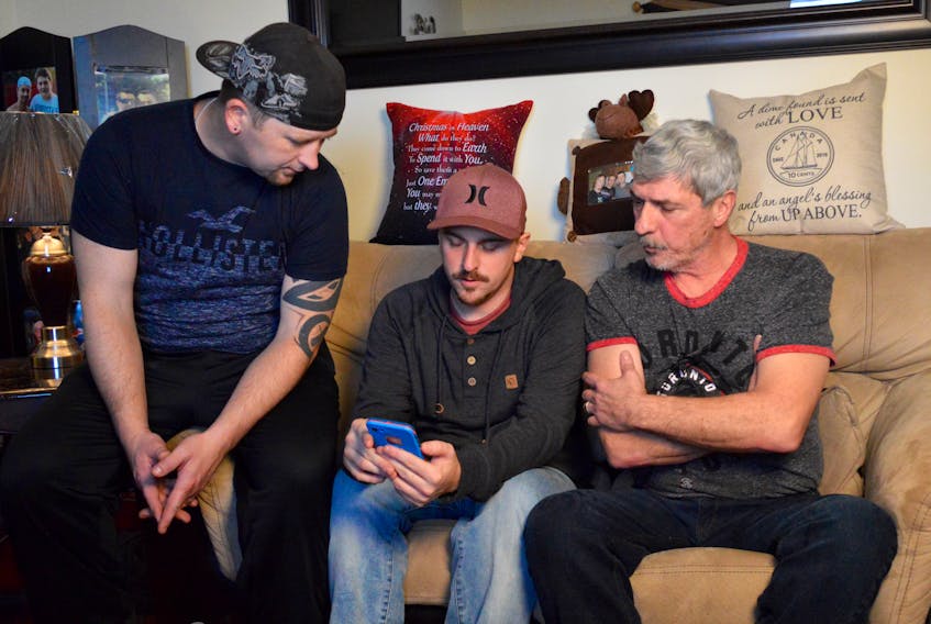 Members of the Williams family look over an email informing them of the charges laid against Nexen Energy, the Alberta-based company that operated the oil sands upgrader facility where 30-year-old Dave Williams was critically injured in an explosion in January 2016. From left, brothers Duke and Archie and their father Michael Williams read the charges that were laid following an extensive investigation by Alberta Occupational Health and Safety. DAVID JALA/CAPE BRETON POST