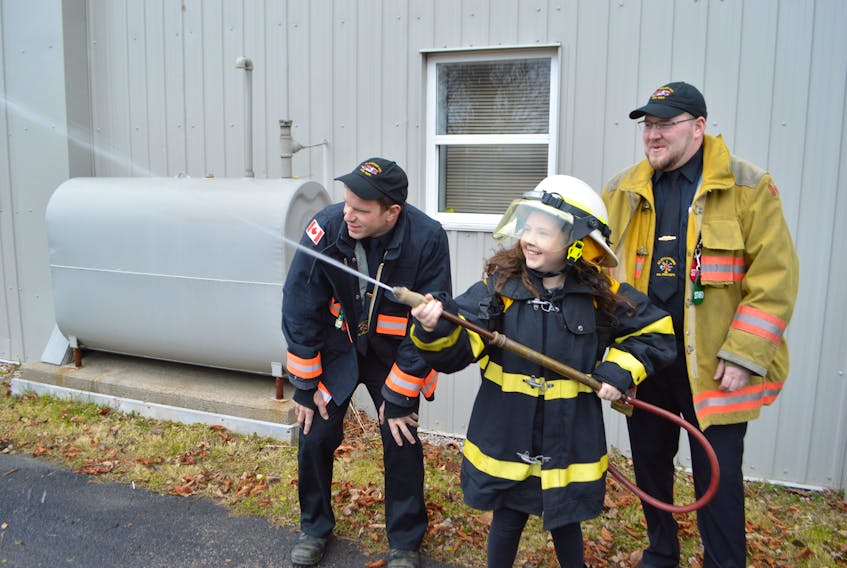 Lucy McKenzie, a Grade 5 student of Greenfield Elementary School in River Ryan, tries out one of the Scotchtown Volunteer Fire Department’s backpack fire hoses, with help from firefighters Evan Boudreau, left,  and Joseph Campbell, while in the role of fire chief for a day at the fire department. McKenzie received the honour as the overall winner in the fire department’s annual fire prevention poster contest.
