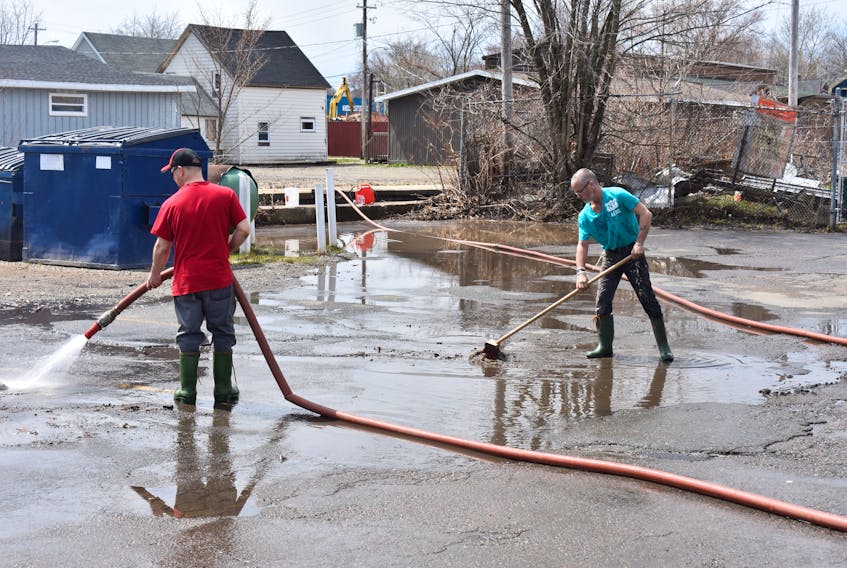 Reggie Harris, left, and Richard Milton work at cleaning up the parking lot of the Steel City Sports Bar and Steakhouse on Monday morning following Sunday’s flooding that threatened the popular Sydney establishment. The workers, who hosed down the parking area, pumped water from the same brook that overflowed the previous day.