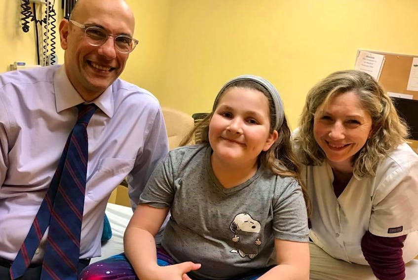 Skyla Bennett, centre, smiles wide after getting a good report from her annual checkup at the Tumour Clinic at the IWK Hospital in Halifax. On the left is her surgeon, Dr. Simon Walling, and his attending nurse is on the right.