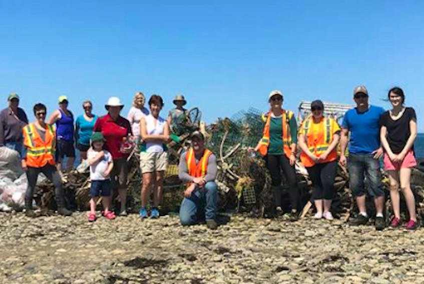 Dylan Yates, kneeling in the centre, and a group of volunteers with the Cape Breton Environmental Association, stand beside piles of trash, broken fishing gear and old tires. The group collected the garbage during a clean-up of Bridgeport Beach they organized for World Ocean’s Day on June 8.