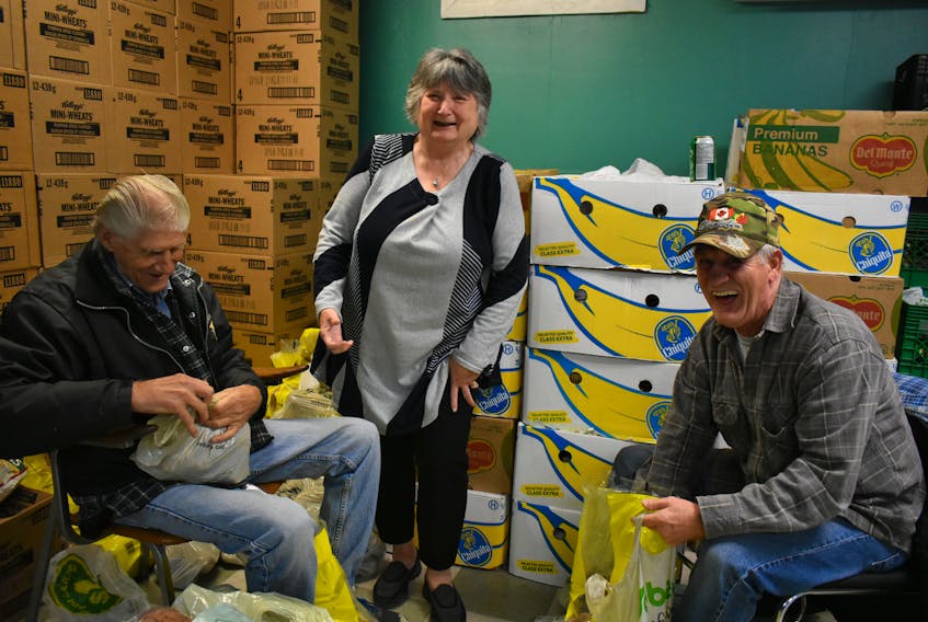 Ruth Martell, centre, shares a laugh with Marvin Boutilier, to her left, and David Burke, to her right, who are bagging potatoes for orders at the Glace Bay Food Bank on Oct. 18. Martell, 70, has been a dedicated volunteer at the food bank for nine years doing client intake and giving hugs when needed.
